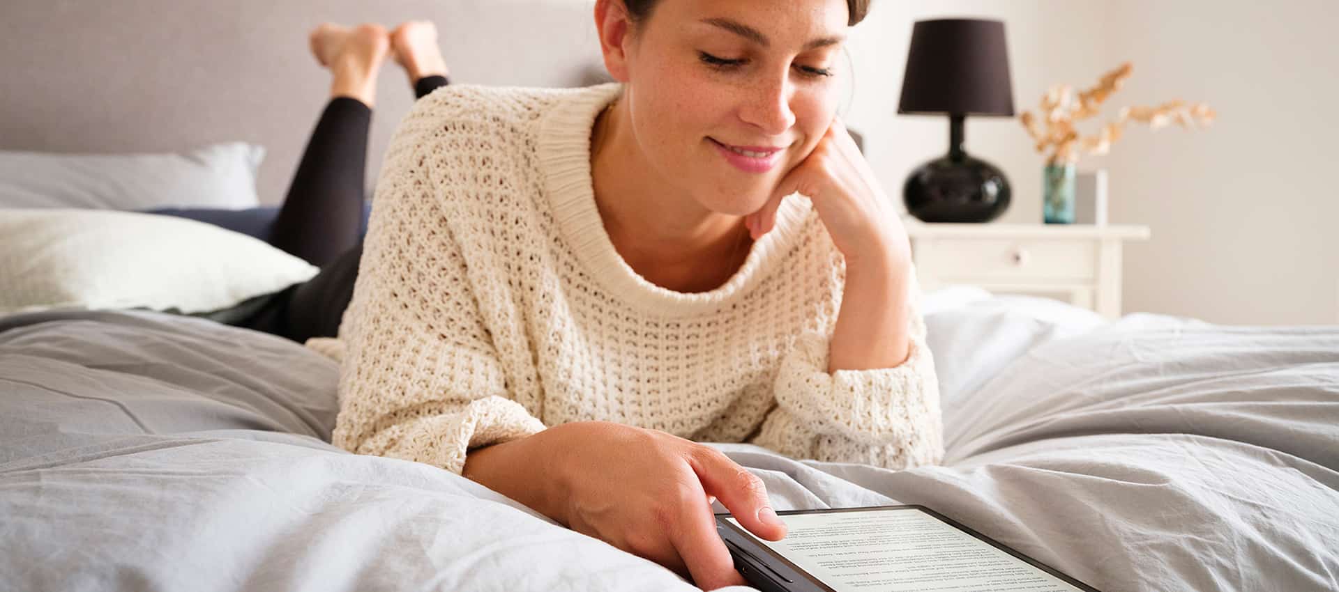 Junge Frau liegt auf Bett und liest auf einem tolino-eReader.